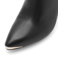 Čierna kožená lodička na vysokom podpätku s špicatou špičkou, s metalickým zlatým akcentom na konci. Textúrovaný povrch s hladkým finišom.