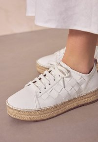 Fehér bőr tornacipő, szőtt oldal részlettel, juta espadrille platform talppal, kerek orral és fűzős rögzítéssel.