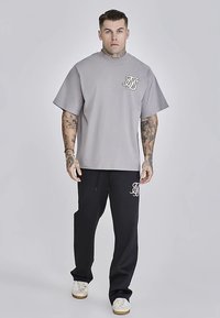 Harmaa lyhythihainen t-paita, jossa on rinnan kohdalla logo, yhdistettynä mustiin collegehousuihin, joissa on pieni valkoinen logo, sekä valkoisiin tennareihin.