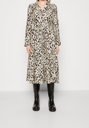 Sukienka midi z długim rękawem i paskiem, z czarno-beżowym abstrakcyjnym wzorem zwierzęcym, noszona z czarnymi skórzanymi kozakami sięgającymi do kolan.
