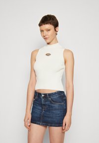 Hvit ribbestrikket ermeløs topp med høy hals og sølvfarget oval detalj, sammen med en mørk blå denim miniskjørt med lommer.