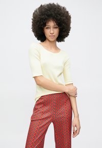 Svetlo rumena oprijeta majica s tremi četrtinami rokavov, združena s črtastimi rdečimi hlačami z diamantnimi vzorci v črni in beli barvi.