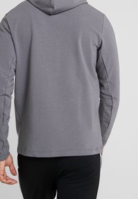 Sweat-shirt à capuche gris à manches longues, texture lisse, et design simple. Présente une coupe décontractée et un ourlet arrondi à l'arrière.