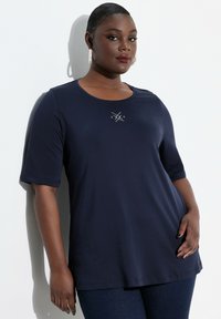 Camiseta de manga corta azul marino con cuello redondo y un patrón bordado metálico en el pecho. Tela suave y lisa con un corte relajado.