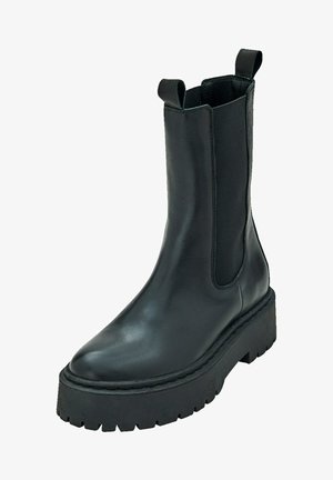 Zwarte leren enkelboot met elastische zijkanten, ronde neus en een dikke, gestructureerde rubberen zool. Beschikt over twee aantrek tabs voor gemakkelijk aan- en uittrekken.