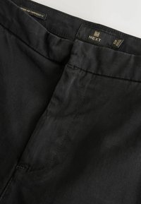 Black tapered fit trousers made from smooth fabric. Features a flat waistband and subtle stitching details. Label reads "NEXT" with size 32R.