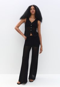 Zwarte gebreide crop top met knopen en bijpassende zwarte wijde broek, met een nettextuur en open weefpatroon.