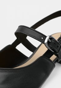 Μαύρο δερμάτινο παπούτσι με κλειστή μύτη και μία λουρίδα με μεταλλική αγκράφα. Η εσωτερική επένδυση έχει ανοιχτόχρωμο αντίθεση.