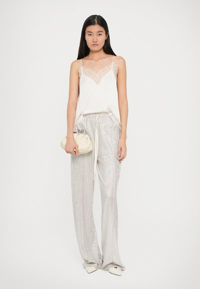 Bluză din mătase cu dantelă albă, asortată cu pantaloni argintii strălucitori cu paiete și o geantă crem tip clutch; pantofi cu vârful ascuțit completează ținuta.
