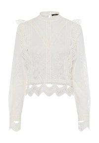 Weiße Spitzbluse mit hohem Kragen, langen Ärmeln, Rüschendetails und gewelltem Saum. Filigrane Blumenmuster heben das Design hervor.