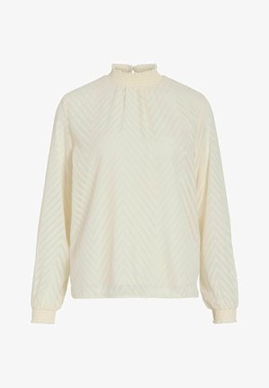 Jasna kremowa bluzka z wysokim marszczonym dekoltem, długimi rękawami i wzorem w jodełkę. Rękawy również są marszczone, co daje efekt marszczenia.