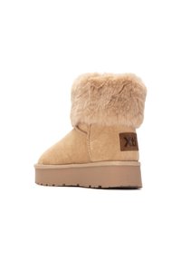 Botín de ante marrón con cuello de piel sintética, suela plana y etiqueta con el logo de Xti. Presenta detalles de costura y material superior texturizado.