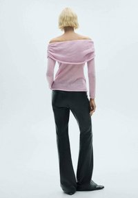 Rosa off-shoulder tröja med draperad tyg, kombinerad med svarta utsvängda byxor och skor med spetsig tå, sedd bakifrån.