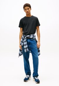 Juoda medvilninė marškinėliai derinami su mėlynais džinsais. Aplinku juosmenį rišama mėlyna ir pilka languota marškinėliai. Mėlyni sportbačiai su baltomis raištelėmis.