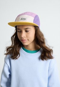 Lila, rosa und cremefarbene Fünf-Panel-Cap mit einem gelben Schirm und einem weißen Etikett mit "LilBoo." Getragen mit einem hellblauen Sweatshirt.
