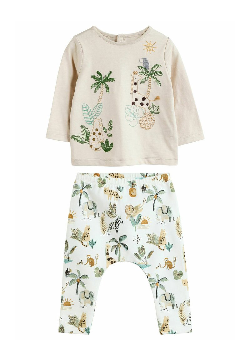 Lichtbeige blouse met lange mouwen en kleurrijke borduursels van dieren en planten, gecombineerd met witte broek met een jungle-thema in gedempte tonen.