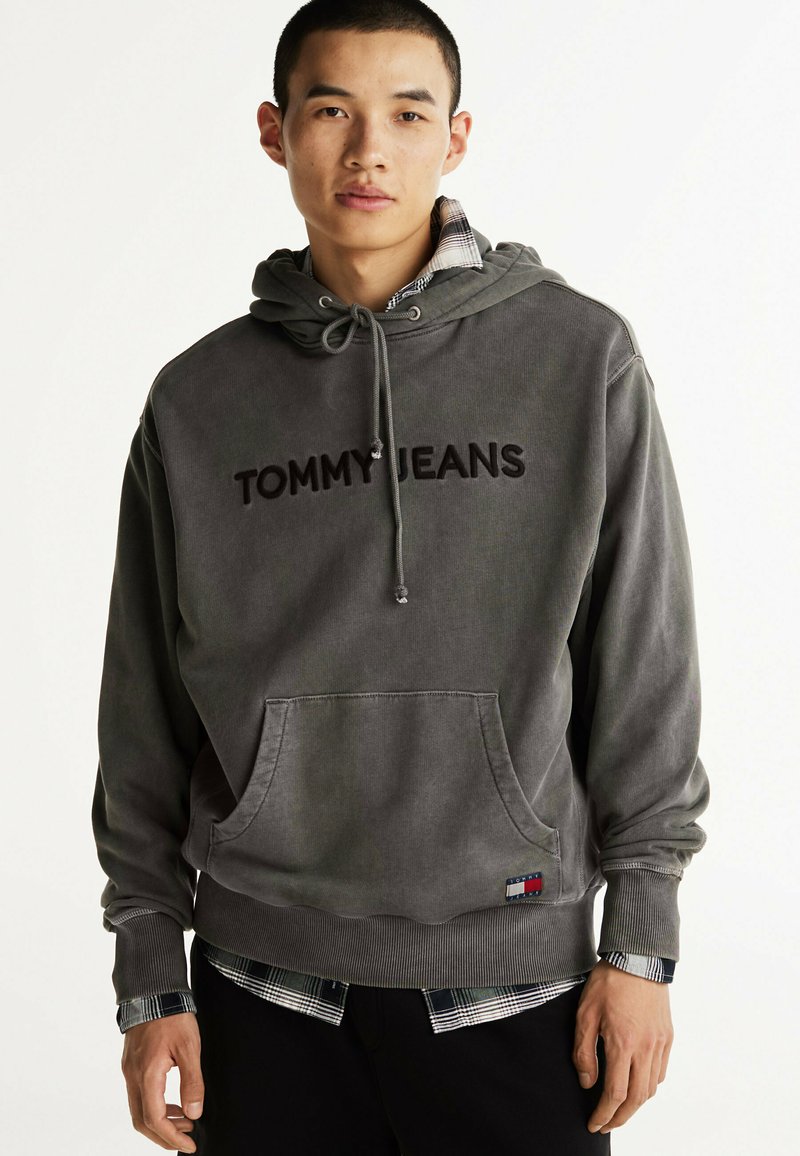 Grau Baumwollhoodie mit "TOMMY JEANS"-Logo, Kordelzugkapuze, Kängurutasche, gerippte Bündchen, unter einem karierten Hemd am Saum.