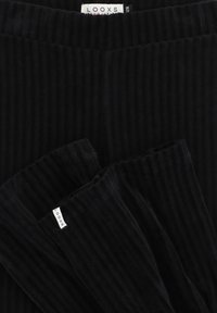 Zwarte corduroy stof met verticale ribbels, gekreukt aan de randen. Aan de naad is een zichtbare merklabel met de naam "LOOXS" bevestigd.