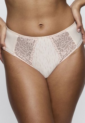 Vrouw draagt lichtroze kanten en satijnen slips met hoge taille, handen rustend op de heupen, toont de middel en bovenbenen.