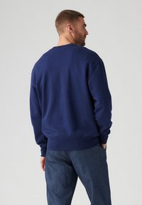 Marineblauwe sweatshirt met geribde boorden en onderrand, voorzien van een ronde hals en een zachte textuur. Draagt met denim broek, gezien vanaf de achterkant.