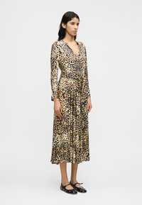 Midi φόρεμα με λεοπάρ σχέδιο, μακριά μανίκια, λαιμόκοψη σε σχήμα V και ζώνη στη μέση. Υφή υφάσματος, ρέουσα σιλουέτα και ελαφρώς φουσκωτό τελείωμα. Μαύρα φλατ παπούτσια.