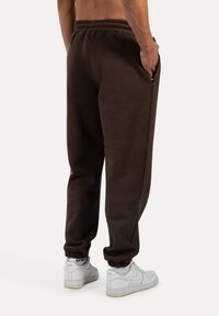 Braune Sweatpants mit lockerer Passform, elastischem Bund und umsäumten Säumen, kombiniert mit weißen Sneakers. Verfügt über seitliche Taschen.