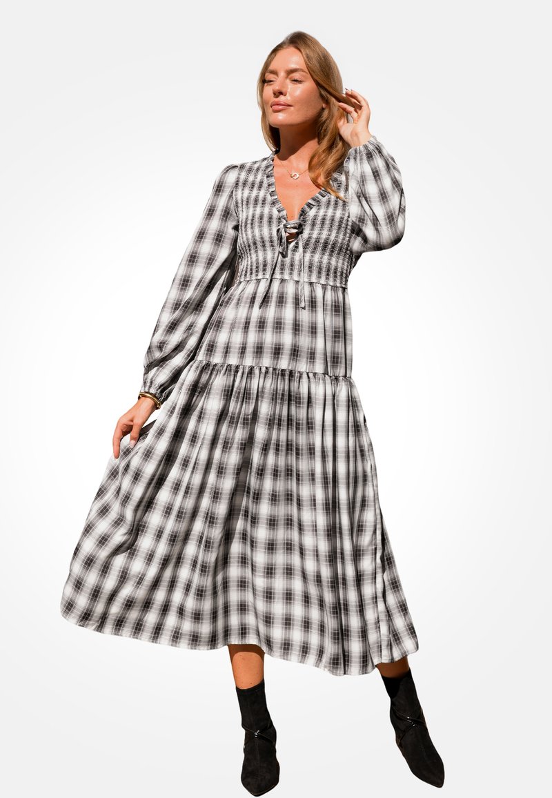 Schwarz-weißer karierter Maxikleid mit langen Ärmeln, gerafftem Oberteil und gestuftem Rockdesign. Getragen mit schwarzen Ankle Boots.