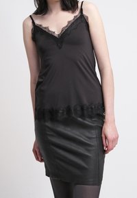 Svart satin camisole med spetsdetaljer vid halsringning och nederkant, tillsammans med en åtsittande svart läderkort klänning. Slät textur genom hela.