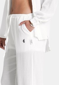 Witte textuuroutfit met een losse top met knopen en bijpassende elastische broek met een zijzak en een klein logo-detail.