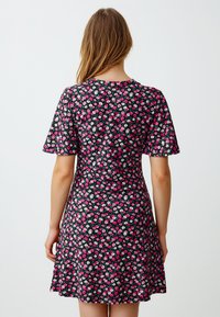 Donna con lunghi capelli che indossa un vestito nero a maniche corte con un piccolo motivo floreale rosa e bianco, vista di spalle.