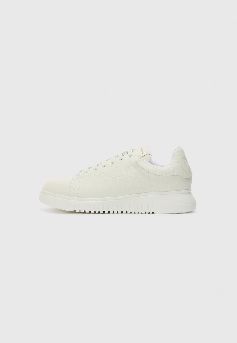 Sapatilha branca em couro com parte superior texturizada, bico arredondado, sola branca plana e cordões tonais. Branding subtil na lingueta.