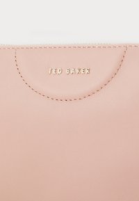 Borsetta in pelle rosa con logo "TED BAKER" in rilievo dorato. Texture liscia e cucitura superiore arrotondata. Presenta dettagli di cucitura sottili.