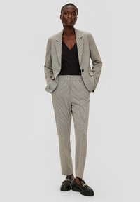 Blazer et pantalon à motif pied-de-poule gris, coupe ajustée. Top noir en dessous, associé à des mocassins noirs épais avec des accents dorés.
