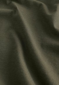 Tissu doux de couleur vert olive avec une texture fine côtelée et des plis délicats créant des variations subtiles de lumière et d'ombre.