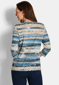 Langarmoberteil mit einem Zickzackmuster in Blau, Beige und Weiß. Der Stoff hat eine weiche Textur, einen Rundhalsausschnitt und eine lockere Passform.