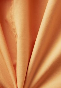 Tissu de couleur pêche douce avec une couture visible, légèrement froncé pour montrer la texture et le tissage lisse.