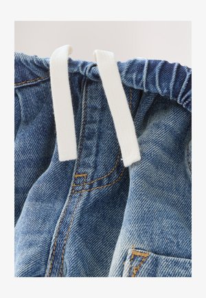 Detailný záber denimu zobrazujúci modrú farbu s vyblednutými časťami, obsahujúci biely šnúrku a viditeľné detaily prešívania.