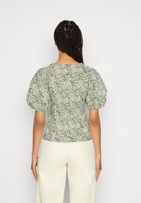 Zielony top w kwiaty o bufiastych rękawach i dopasowanym kroju, wykonany z teksturowanej tkaniny z białym wzorem róż.