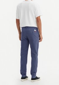 Tmavě modré bavlněné chino kalhoty s úzkým střihem, vybavené dvěma zadními kapsami a jemnou logovou nášivkou, spárované s bílým tričkem a černými teniskami.