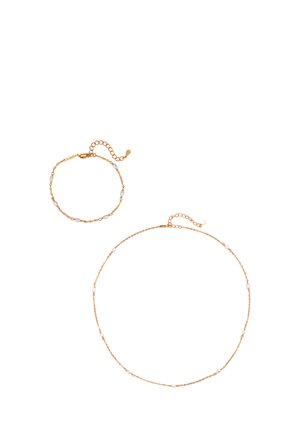 Zarte goldene Gliederhalskette und passendes Armband mit kleinen weißen Perlenakzenten und verstellbaren Verschlüssen vor weißem Hintergrund.