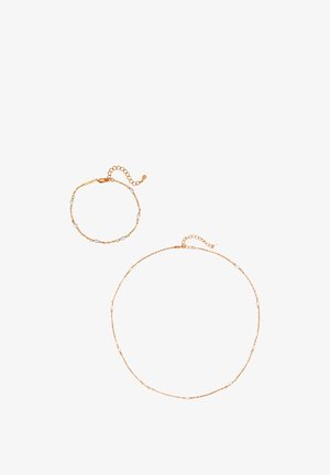 Delicate gouden ketting en bijpassende armband met kleine witte parelaccenten en verstelbare sluitingen op witte achtergrond.