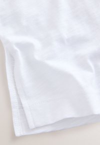 Tessuto bianco, che mostra una texture morbida, con orli arrotolati e pieghe delicate. Il materiale sembra leggero e traspirante.