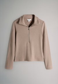 Beige geribd shirt met lange mouwen, halve rits aan de voorkant en omgeslagen kraag, plat weergegeven tegen een lichtgrijze achtergrond.