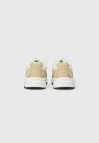 Zapatillas con una combinación de colores beige y blanca, que presentan una parte trasera texturizada, un collar acolchado y una suela gruesa blanca con detalles en negro.