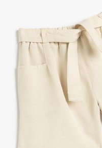 Beige-linjakorte, joissa on keräilty vyötärö, sidottava vyö ja kaksi sivutaskua, valmistettu pehmeästä ja teksturoidusta kankaasta.