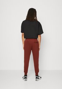 Svart kortärmad topp i kombination med vinröda jogger-byxor som har en bakficka. Modellen bär svarta och vita sportskor.