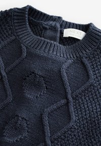 Granatowy sweter dzianinowy z fakturowanymi wzorami, prążkowanym okrągłym dekoltem i widoczną metką marki. Posiada różnorodne wzory ściegów i wypukłe akcenty.