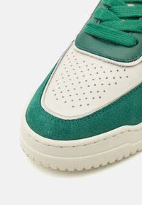 Baskets en daim et cuir vert avec bout perforé blanc, languette rembourrée et semelle en caoutchouc épaisse. Dotées de lacets verts et de coutures discrètes.
