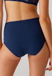 Marineblauwe katoenen high-waisted slipjes met een golfvormige kantafwerking langs de tailleband en beenopeningen, een gladde textuur en een volledig dekkend ontwerp.