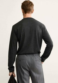 Maglietta nera a maniche lunghe con collo rotondo, abbinata a pantaloni eleganti grigi con tasche laterali, mostrando una trama liscia e una vestibilità su misura.